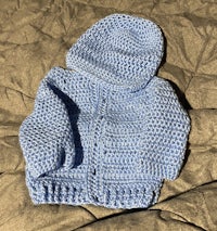 a blue crocheted baby jacket laying on a bed