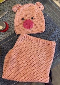 a crocheted pig hat and blanket on a cutting board