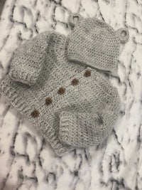 a grey knitted bear cardigan and hat on a marble table